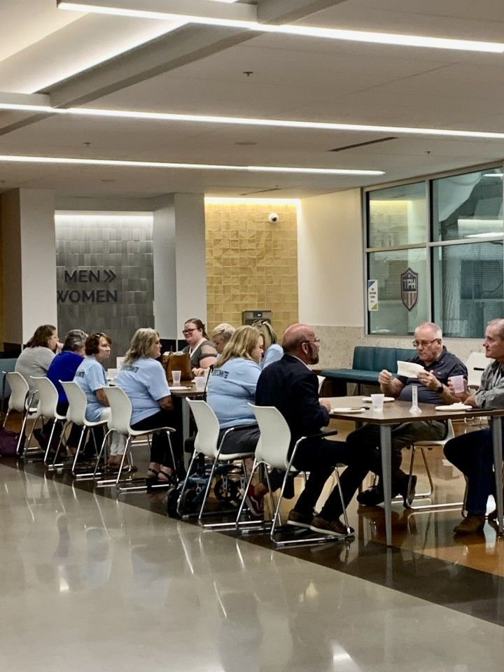 People sit at tables in a brightly lit room. Some wear matching blue shirts