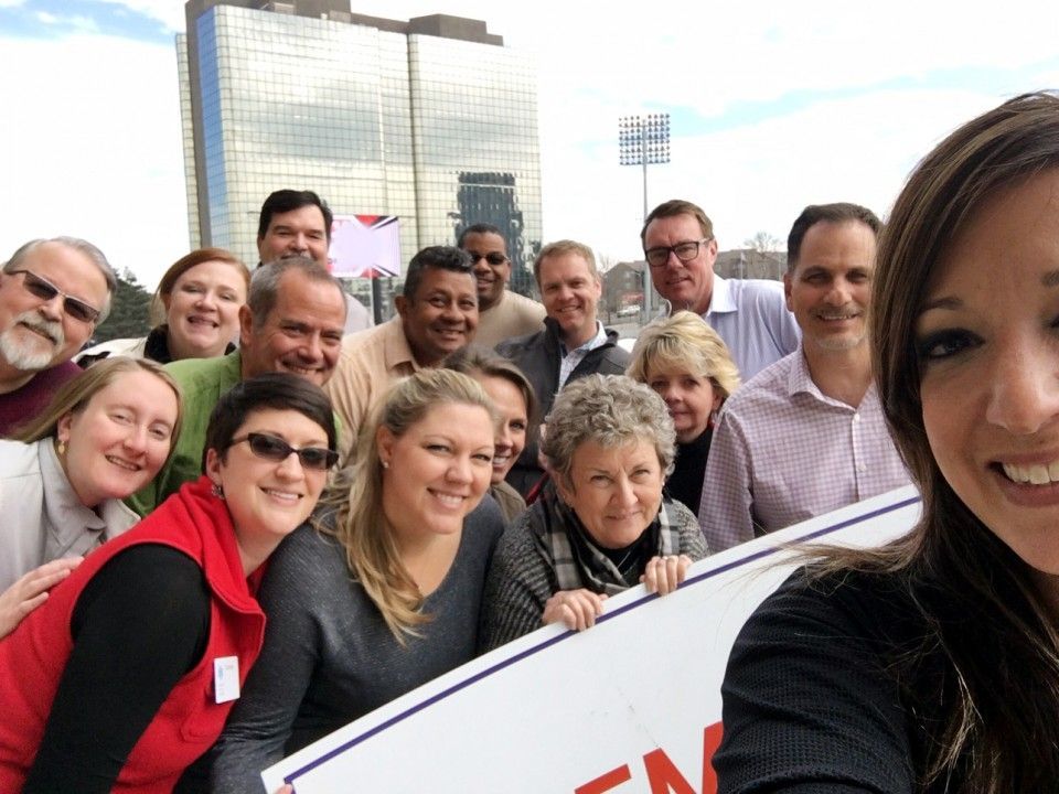 Group of people smiling for a selfie outdoors, in front of a tall building.