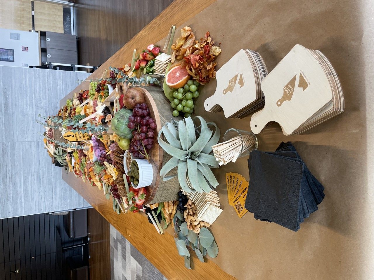 A large charcuterie board with fruit, crackers, and cheese, next to small wooden serving boards.