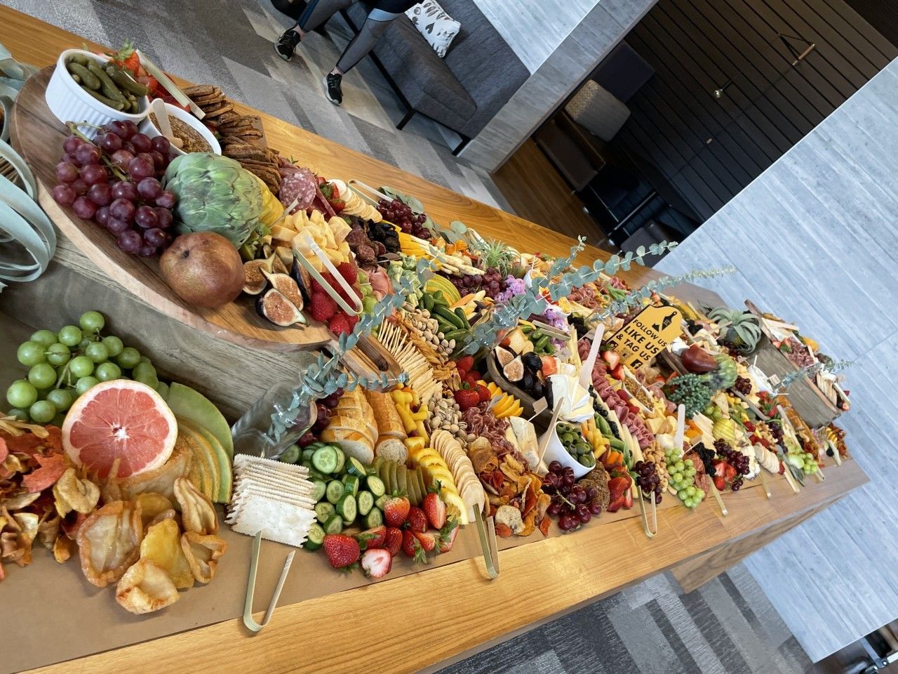 Charcuterie board laden with fruits, cheeses, crackers, and snacks, arranged on a long wooden table.