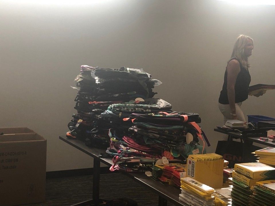 Woman sorting items at a table with a large stack of folded textiles. Cardboard box and other items are nearby.