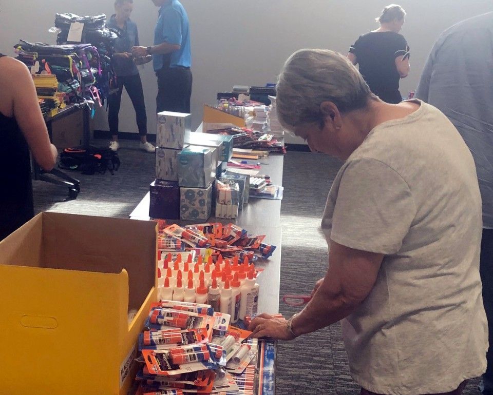 Person looking at glue sticks on a table at a school supply giveaway event.