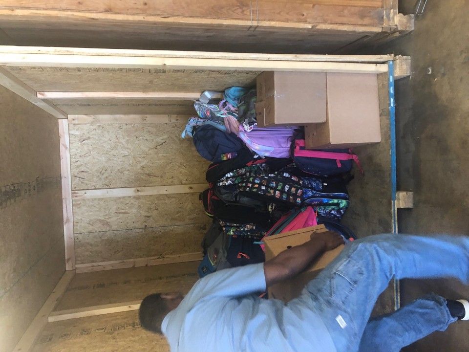 Man loading backpacks and boxes inside a wooden crate.