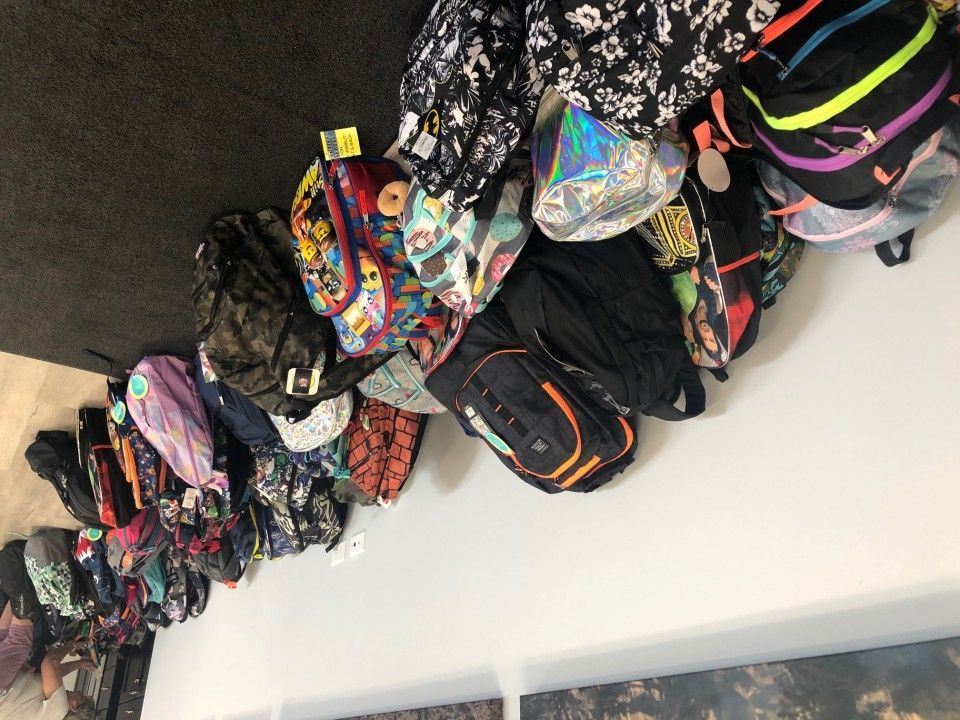 A collection of backpacks in various colors and patterns displayed on a white wall.