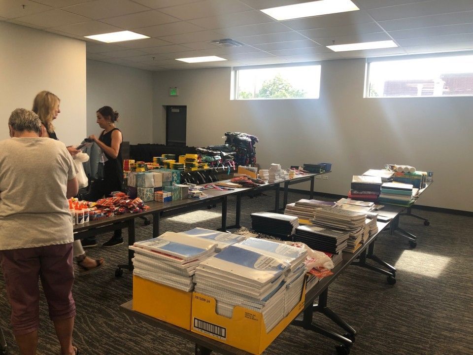 People sorting supplies at tables in a brightly lit room. Boxes and various items are spread out.