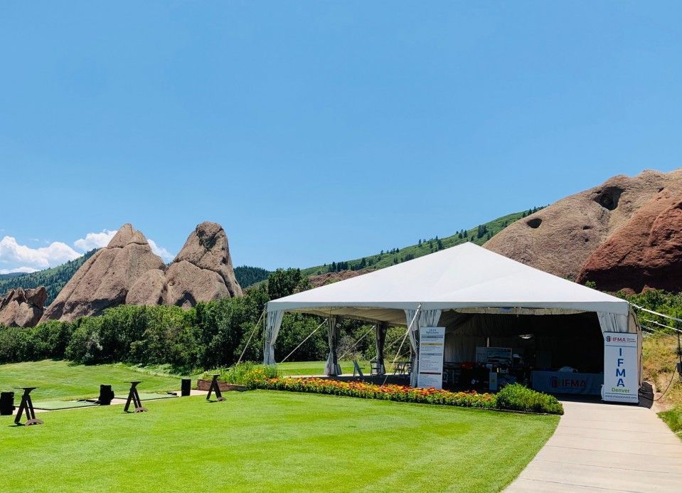 White tent on a green lawn with red rock formations and a blue sky in the background.