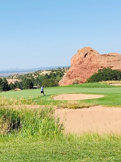 Golfer on green, sand trap in front. Red rock formation in background. Sunny day.
