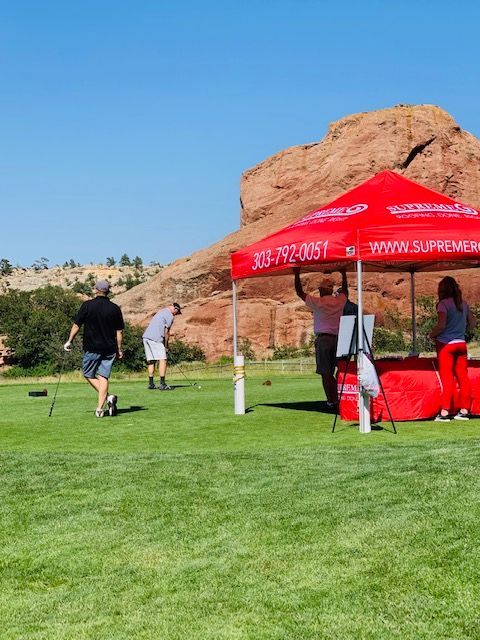People playing a game on green grass with a red tent in front of a red rock formation under a blue sky.