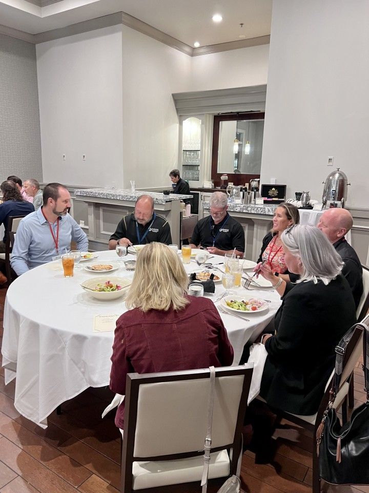 People seated around a large round table, likely at a business or conference event, eating and conversing.