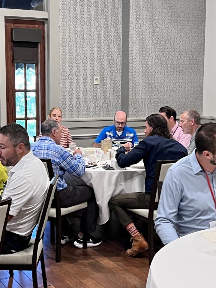 People seated around a table, engaging in a conversation at an event in a room with patterned walls.
