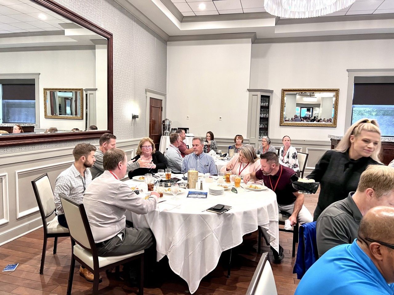 People gathered around a round table in a banquet hall, some eating and talking.