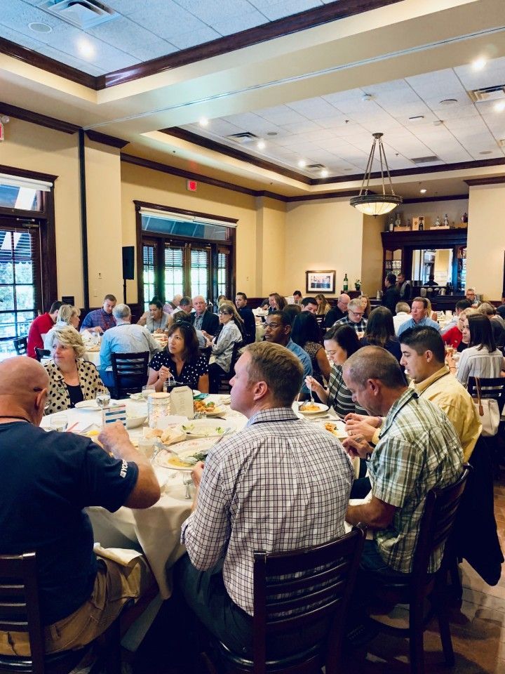 People seated around tables eating in a restaurant. Sunlight streams in.