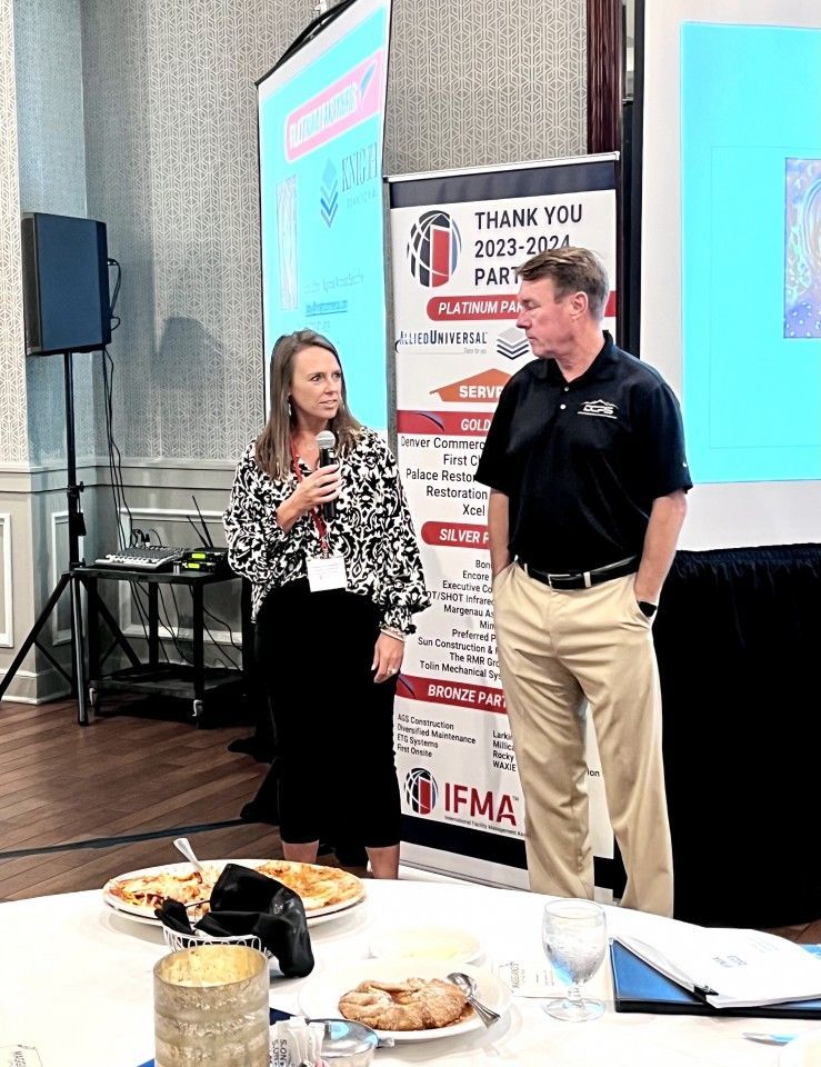 Two people speaking at an event, near a banner that says