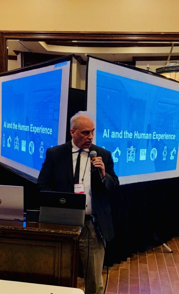 Man speaking into microphone at a conference with screens displaying 