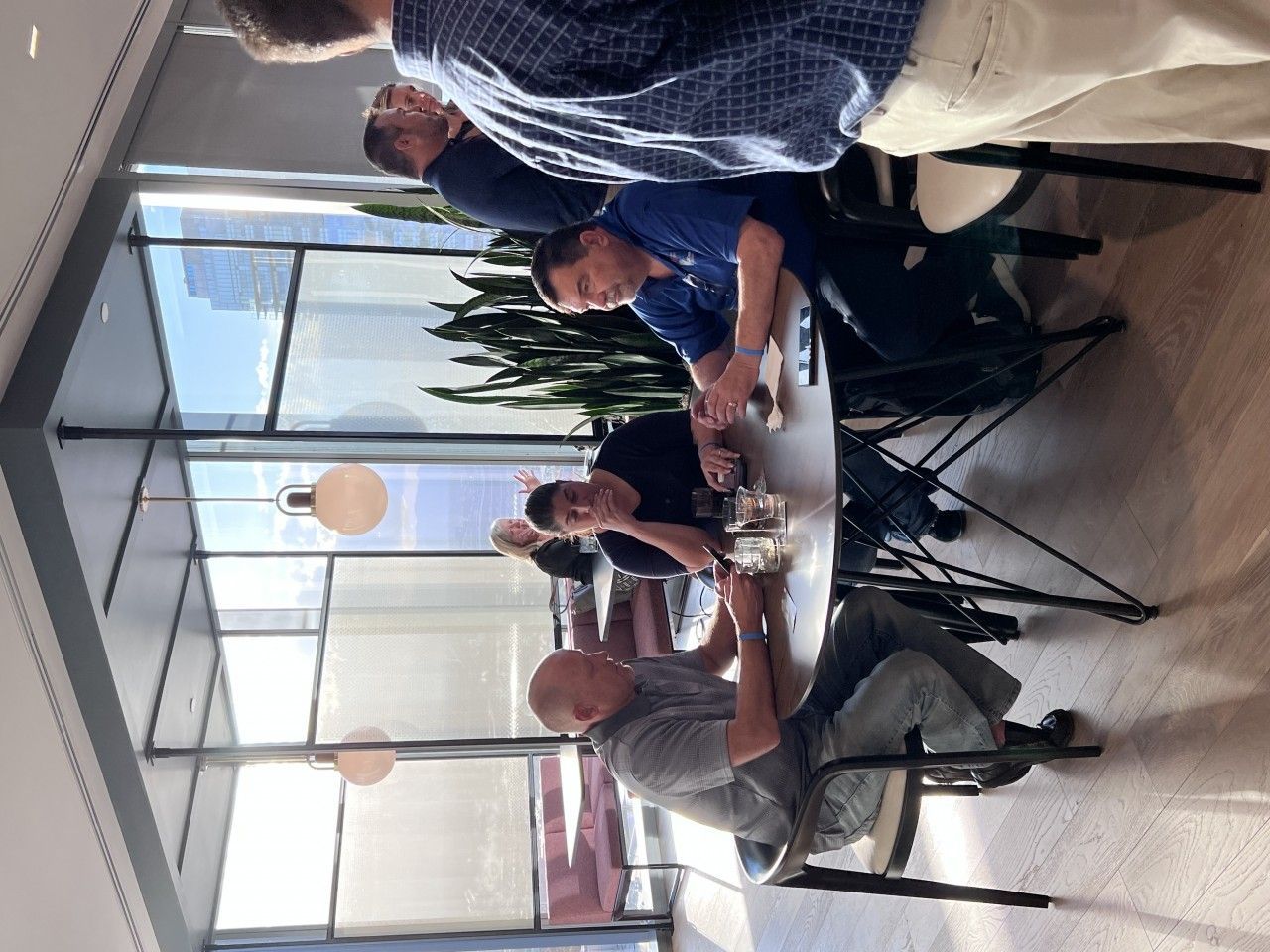 People gathered around a white table, toasting drinks near a large window.