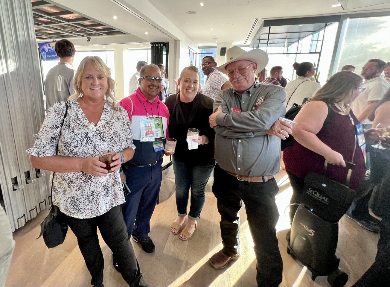 Four people in a room, smiling. A woman in a cowbow hat smiles next to two women and a person with a pink shirt.