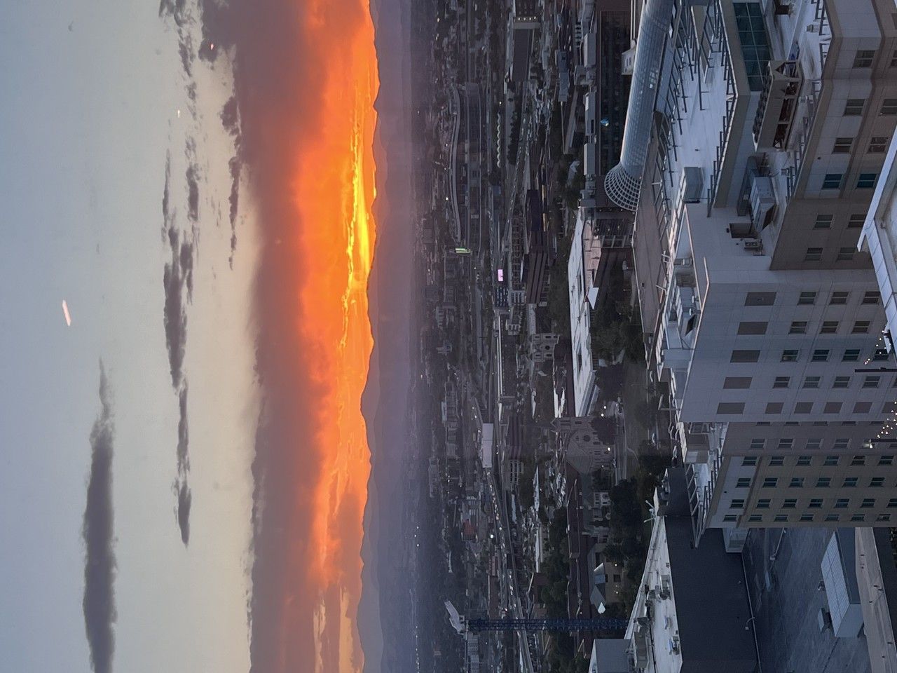 Sunset over a city skyline with orange and yellow hues, viewed from a high-rise building.
