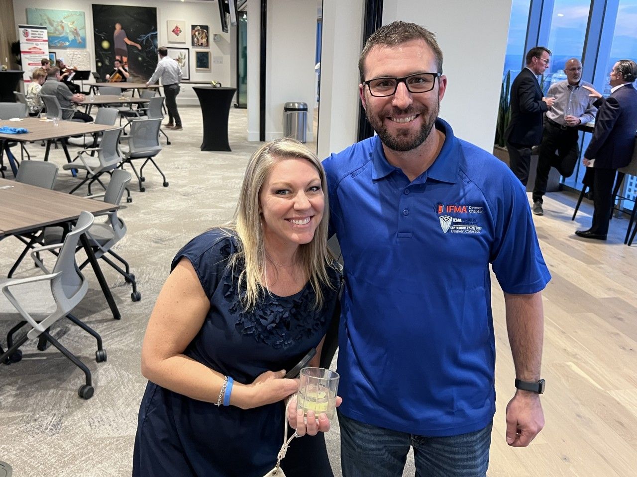Woman in navy dress and man in blue polo smile, posing for photo indoors.
