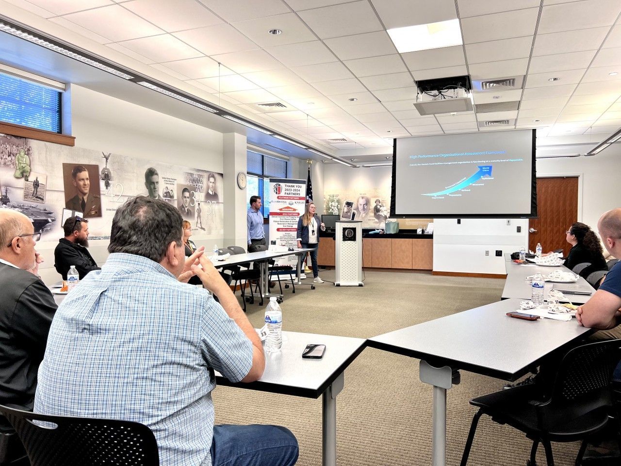 People attending a presentation in a meeting room. A screen displays a graph.