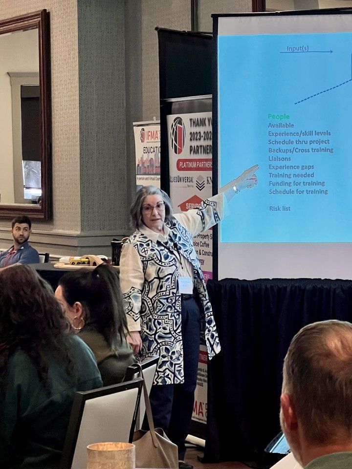 Woman presenting at a conference, pointing to a slide with text. People in the audience.
