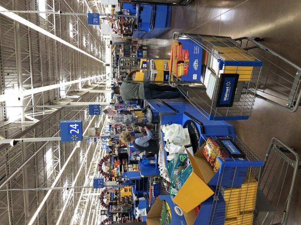 Checkout lanes at a Walmart store. Shoppers and cashiers are visible. Fluorescent lights and a high ceiling.