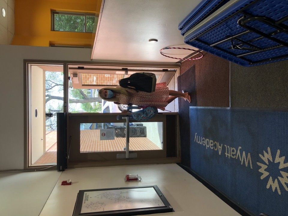 Woman entering Wyatt Academy school door, wearing a mask, backpack. Blue welcome mat.