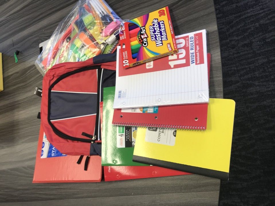 Backpack overflowing with school supplies: notebooks, folders, crayons, and a kite.