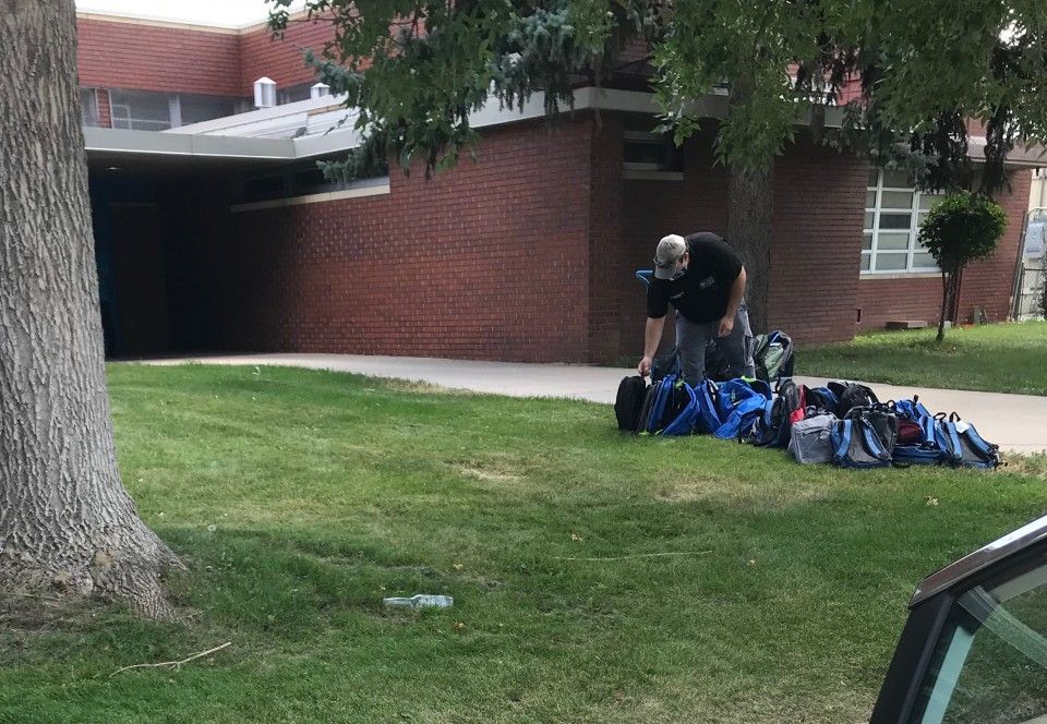 Man organizing backpacks on a lawn in front of a brick building with a covered entrance.