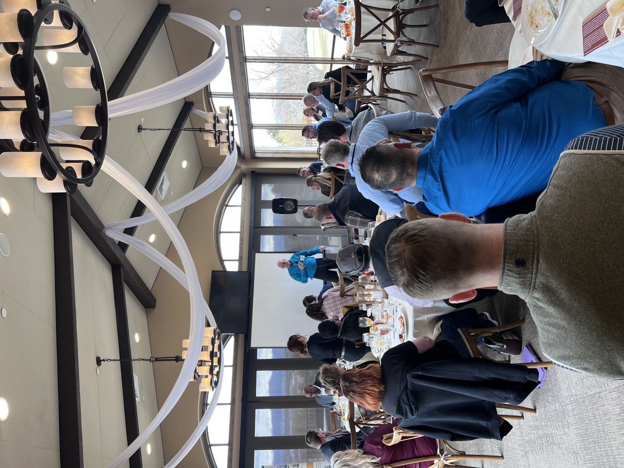 People at a gathering in a room with large windows, tables, and decorations.