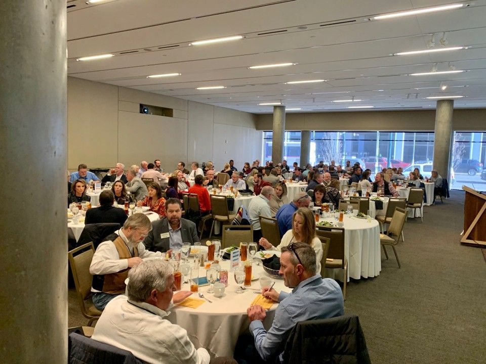 Large room with round tables; many people are seated, eating and talking.