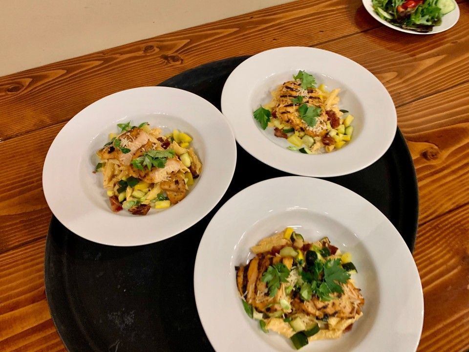 Three white plates of chicken salad on a black tray atop a wooden table.