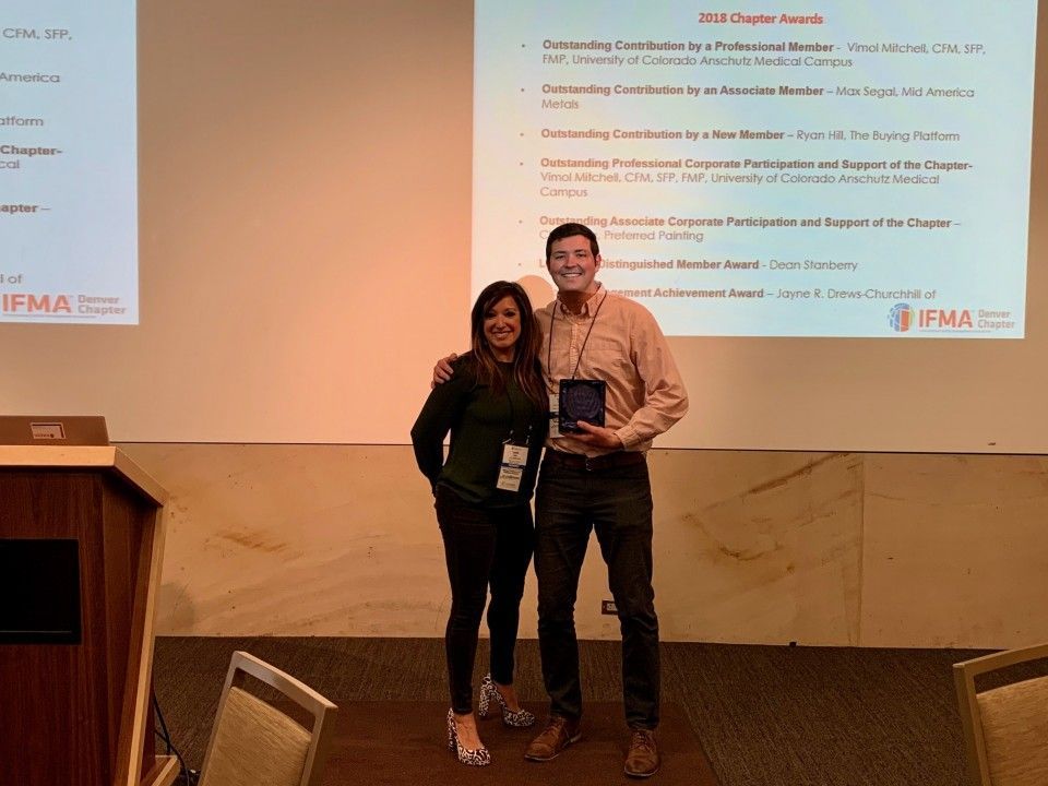 Woman and man holding award, standing in front of a presentation screen, smiling.