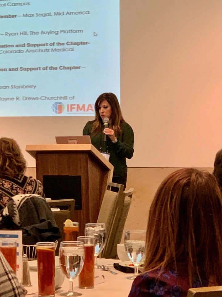 A woman speaks at a podium during a conference, with a presentation screen behind her.