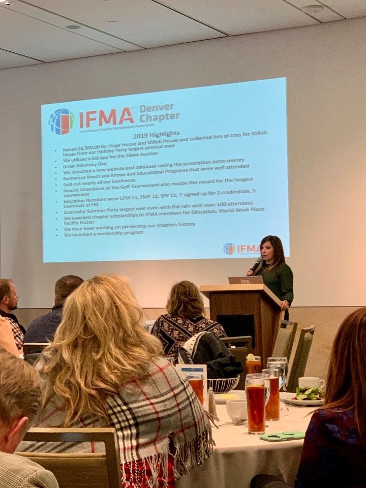 Woman presenting at IFMA Denver Chapter event, with screen displaying text; audience seated at tables.