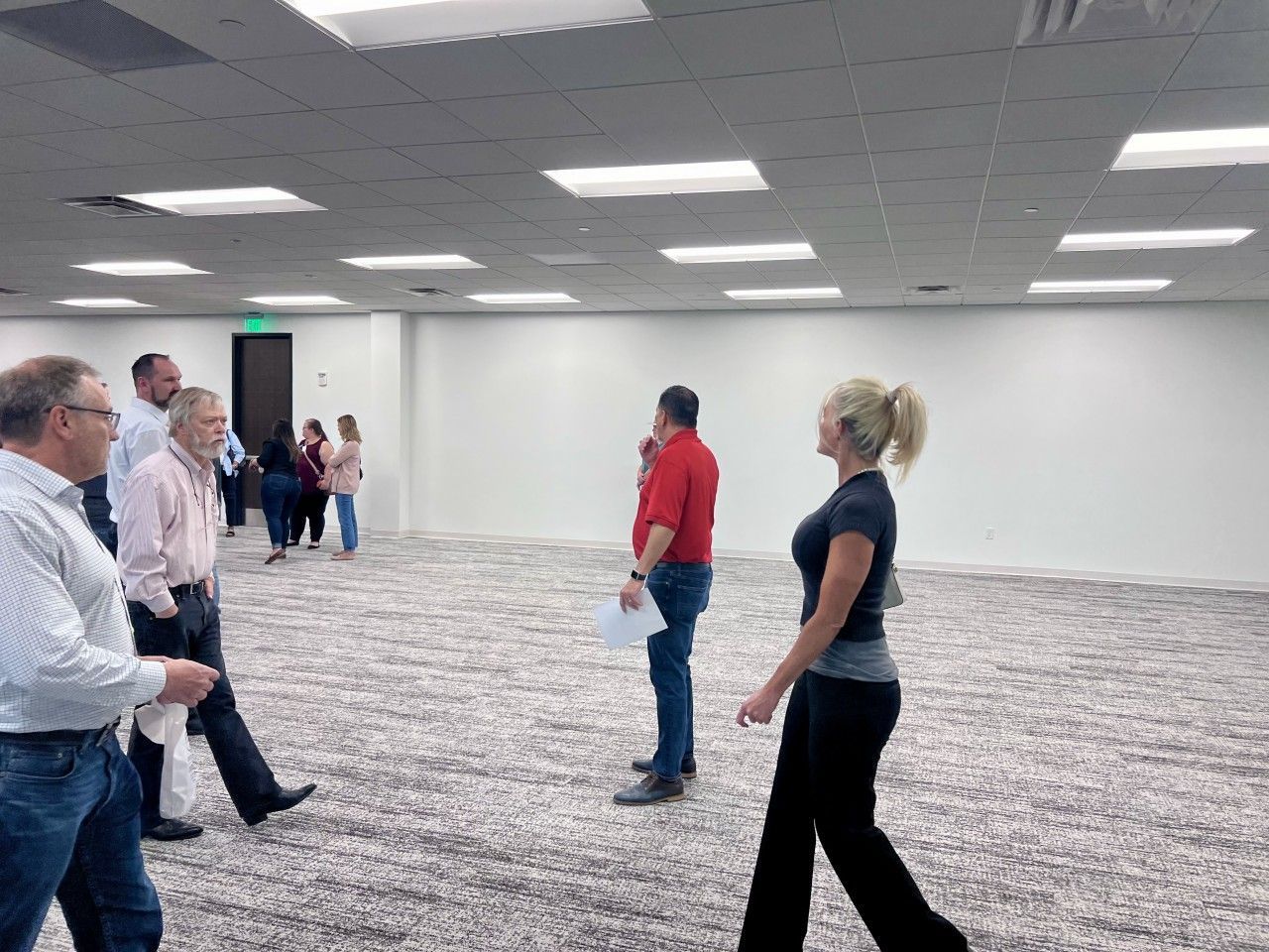 People in a bright room with light fixtures. One person in a red shirt, another in black, with several others present.