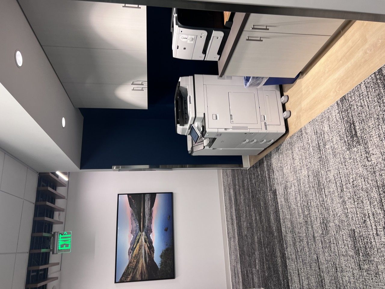 Office space with printer, cabinets, artwork, and an exit sign.