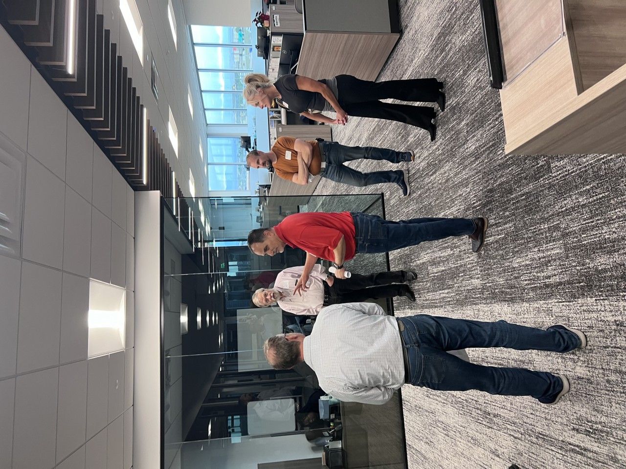 Five people standing in an office. They are posing in front of windows with office cubicles.