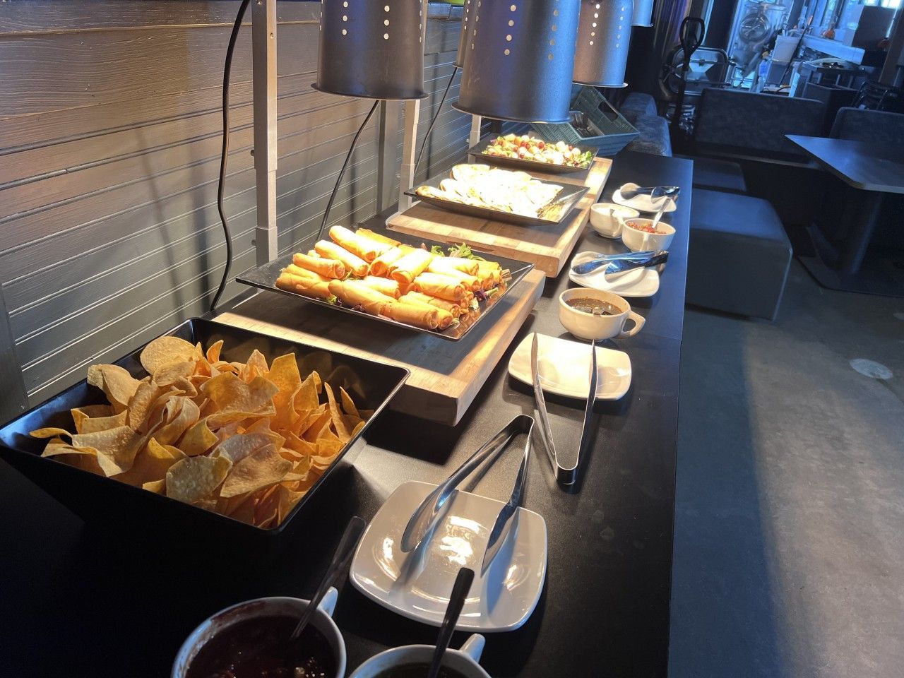 Buffet with various foods, including chips, taquitos, and other dishes under warming lamps.
