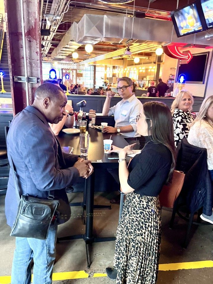 People standing and talking in a bar. One man gestures with his hand.