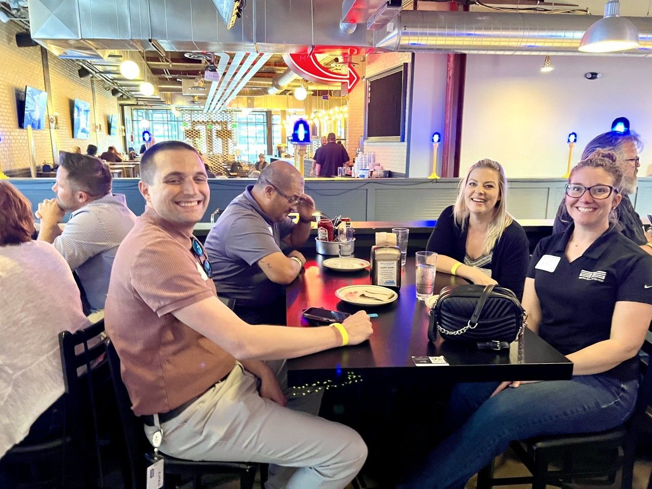 People seated at a table in a restaurant, smiling. Man in brown shirt, woman in black shirt.