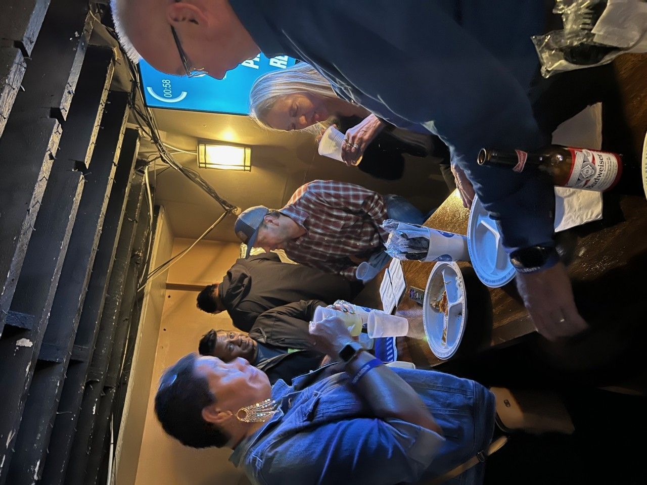 People gathered, possibly in a bar or narrow space, eating and talking.