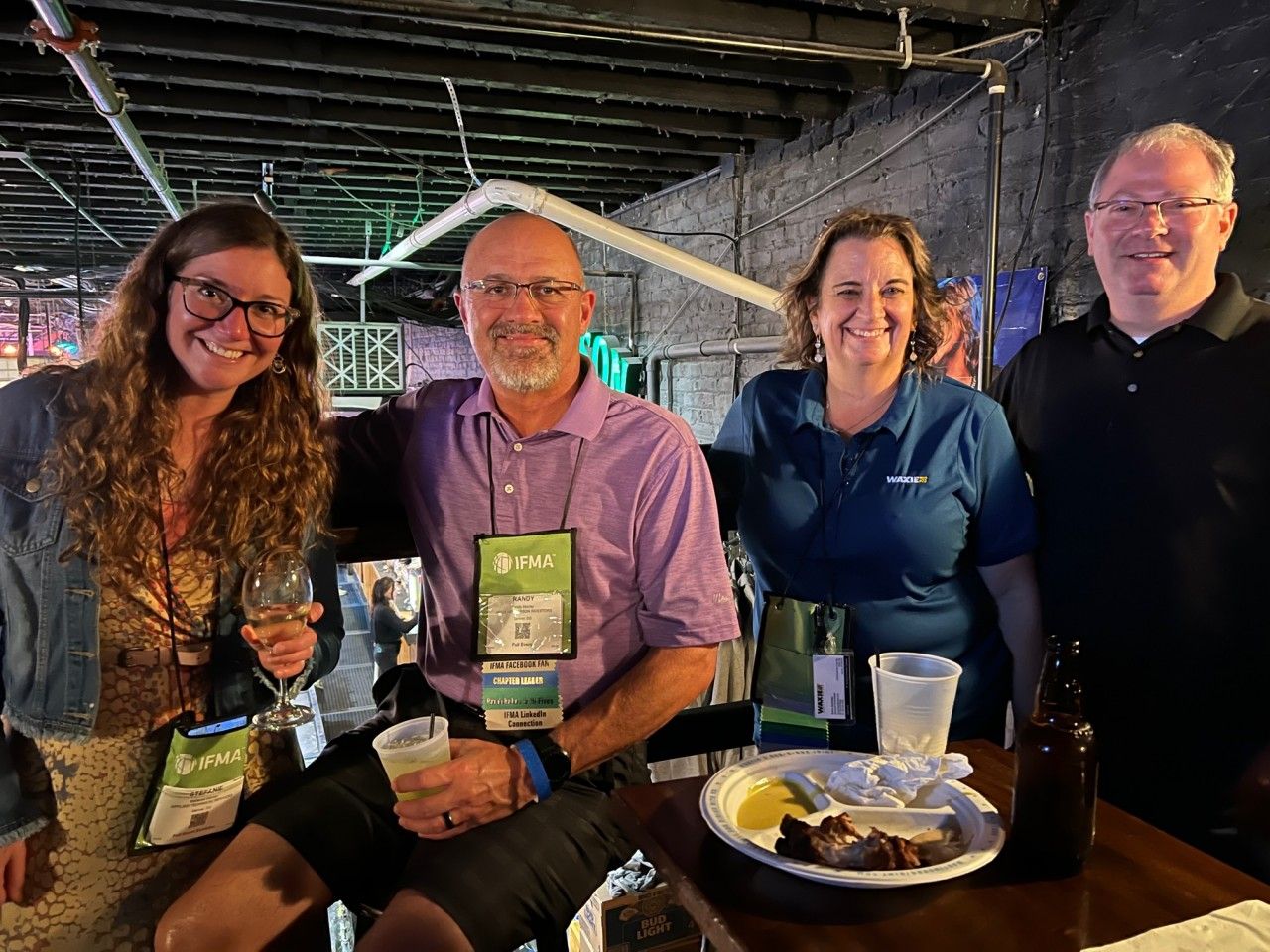 Four people smiling and gathered around a table with drinks and snacks.