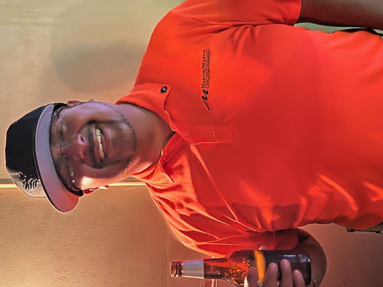 Person in orange shirt and hat smiles while pouring drink from a bottle.