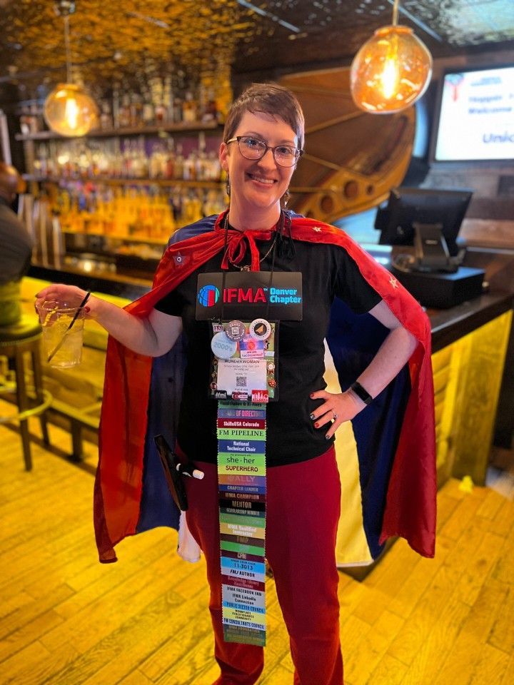 Woman wearing cape and badge lanyard in a bar, smiling.
