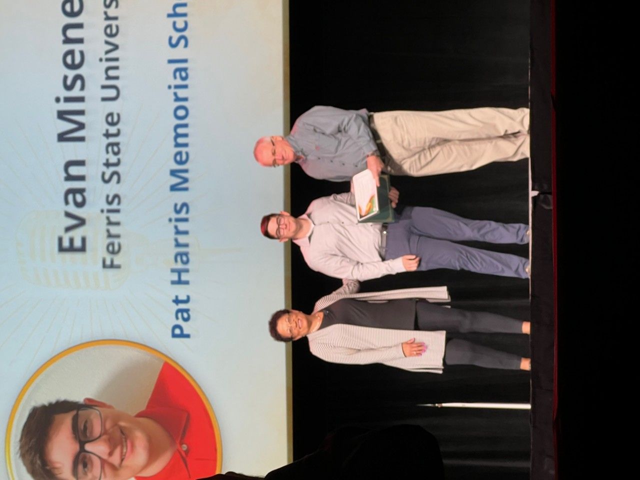 Evan Misener at Pat Harris Memorial School receives an award from two people on a stage.