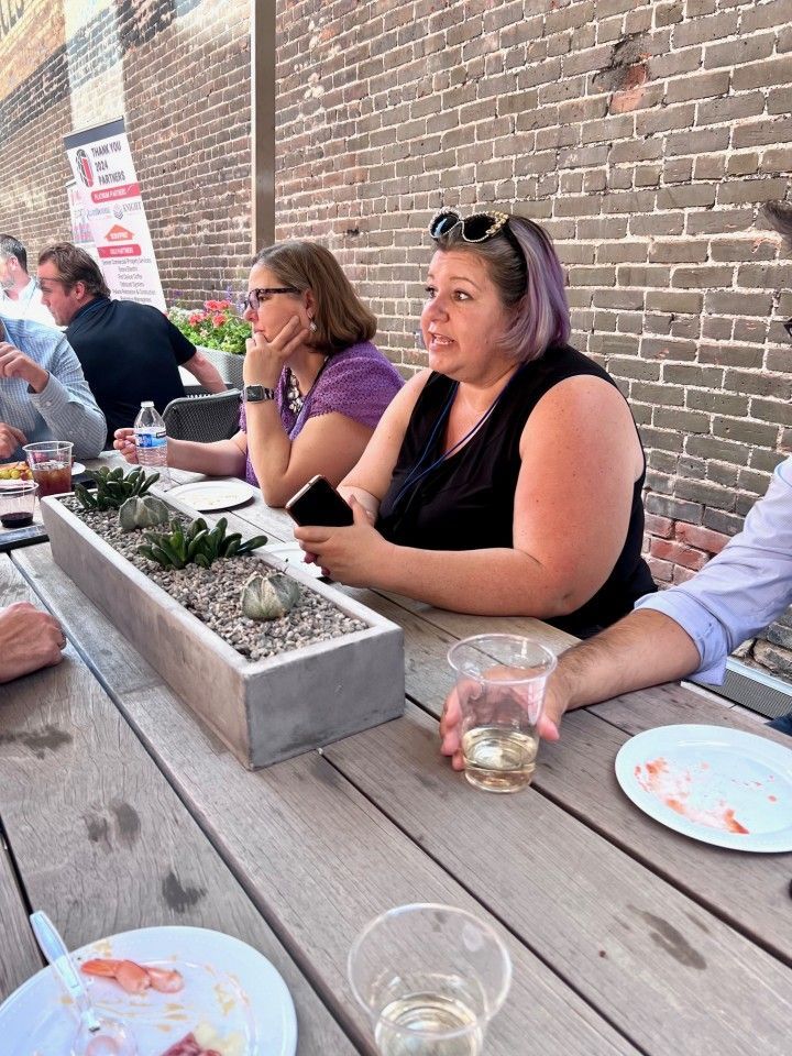 People seated at a wooden table outdoors, engaged in conversation.
