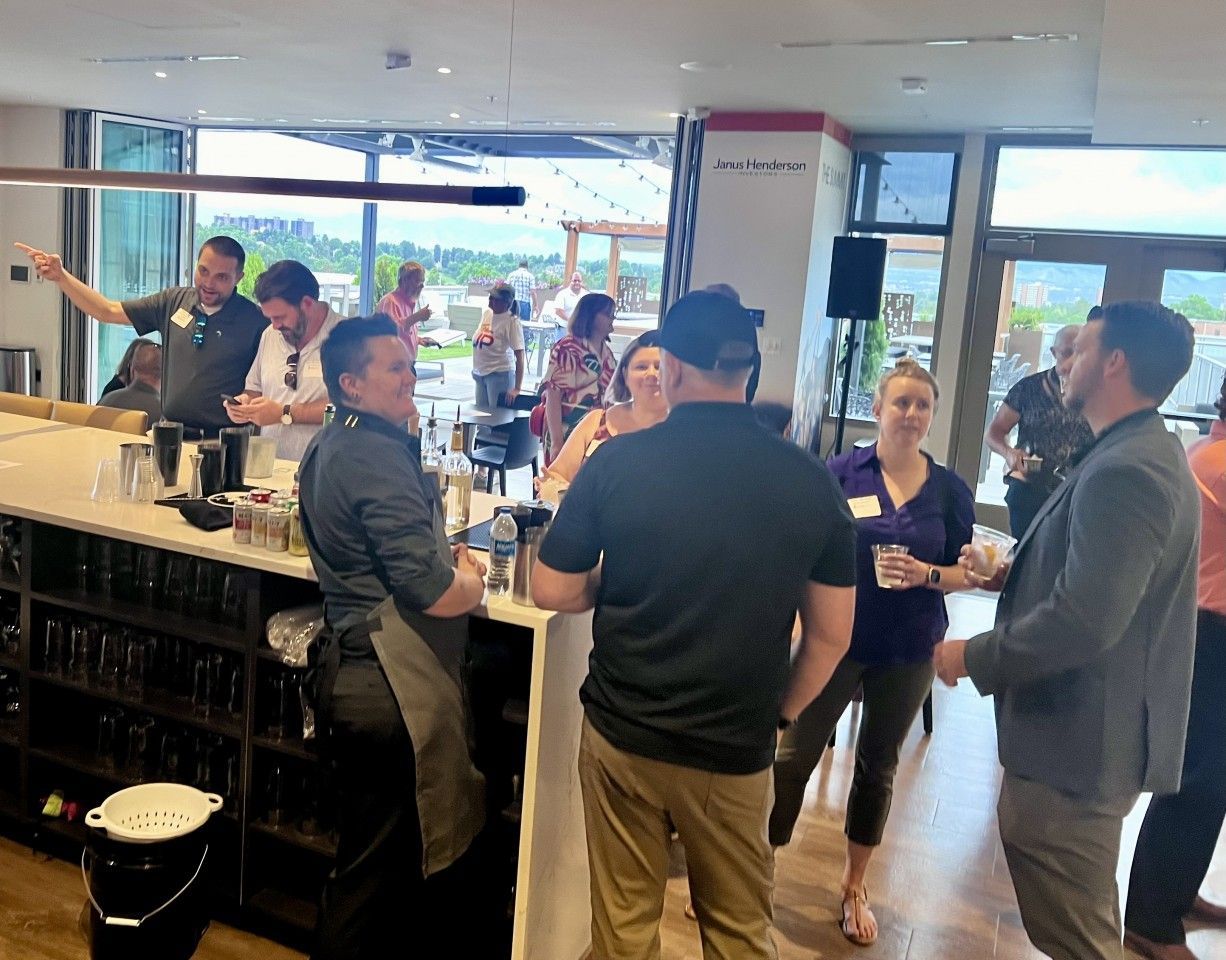 People at a bar, some talking, others near bartender. Outdoor patio visible.