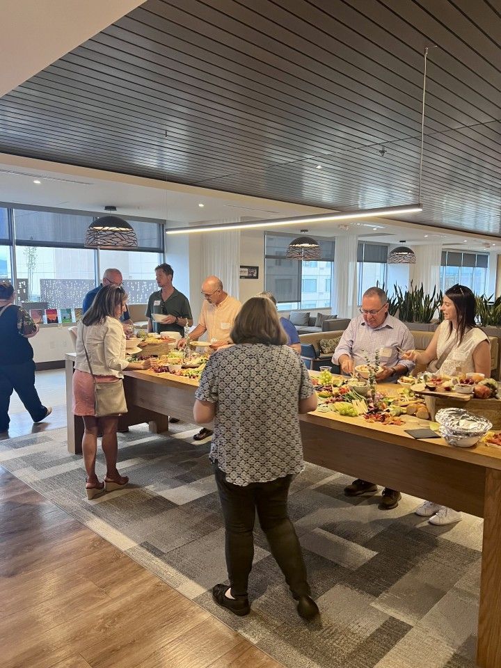 People at a buffet table in a modern office space, selecting food.