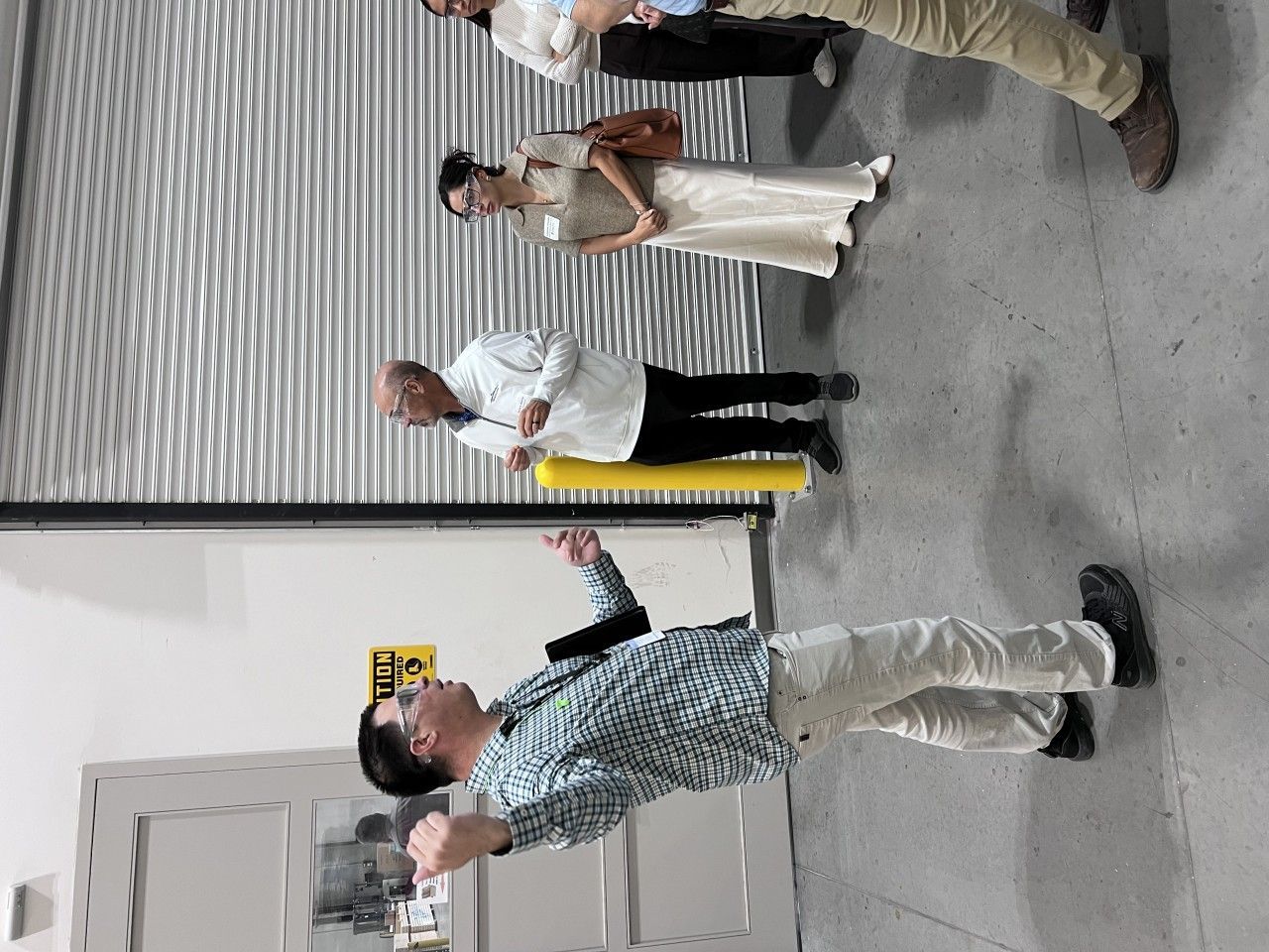 Group of people at a building entrance; man gesturing, others looking on. Light colors.