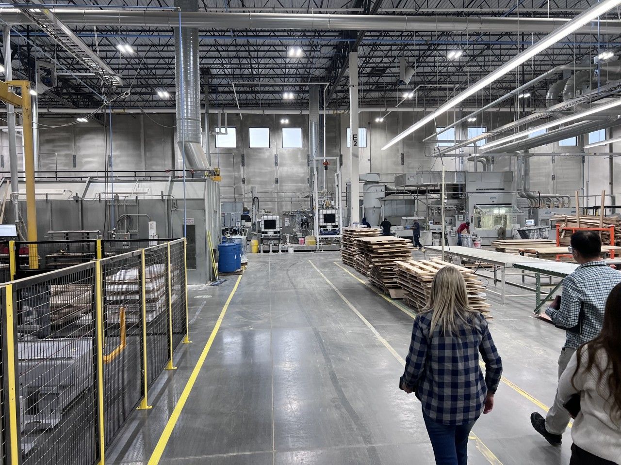 People touring a factory with industrial machinery and wood.